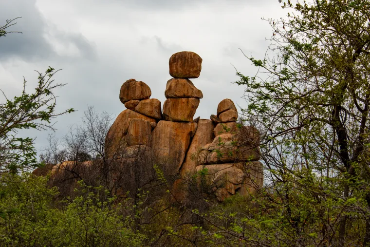 Balanced granite boulders among trees under a cloudy sky