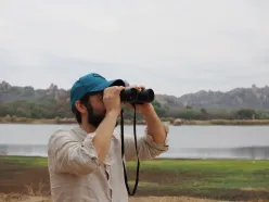 Phillip Wenzel in profile, scanning a body of water with binoculars