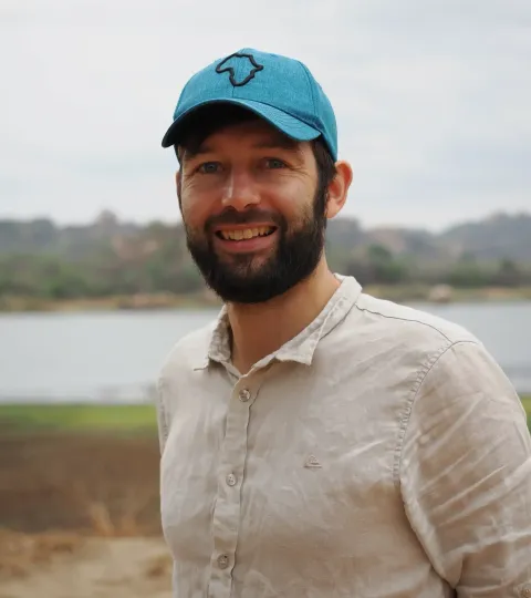 Phillip Wenzel wearing a cap in front of a reservoir, smiling at the camera