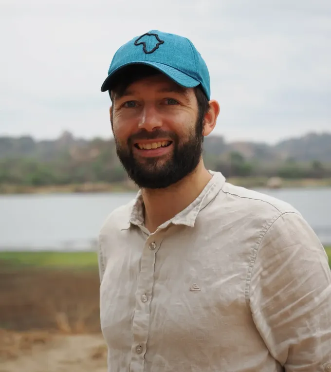 Phillip Wenzel wearing a cap in front of a reservoir, smiling at the camera
